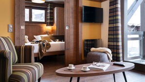 Habitación de hotel con cama, sofá, una mesita con tazas y un mando a distancia, y televisión en la pared.