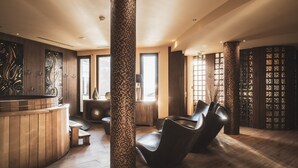 Zona de spa con pisos de madera, una camilla de masaje, una recepción y un pilar con mosaicos.