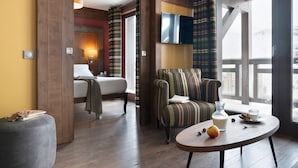 A hotel room with a bed, a sofa, a table with fruit and a glass, and a TV on the wall. - T3 avec vue imprenable | Piscine sur place & spa (Val Thorens)