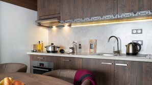 A modern kitchen with wooden cabinets, a stainless steel sink, and a dining area with a table set for two. - T3 avec vue imprenable | Piscine sur place & spa (Val Thorens)