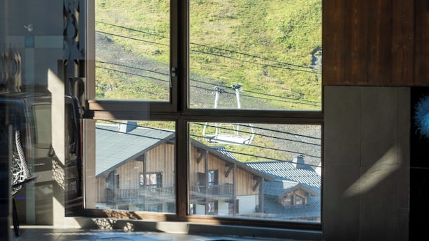 A room with a large window overlooking a mountainous landscape, a wooden interior, and a reflection in the glass. - T3 avec vue imprenable | Piscine sur place & spa (Val Thorens)