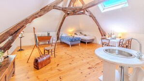 Acogedor dormitorio en ático con techo inclinado, estructura de vigas de madera, cama, escritorio, silla, mesita pequeña, lámpara y ventana.