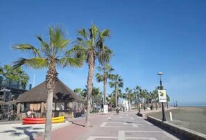 Un sendero frente a la playa bordeado de palmeras, un edificio con techo de paja y un cartel.