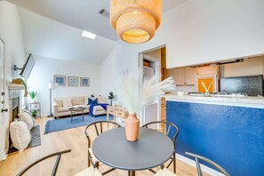 Eine moderne Küche mit blauer Akzentwand, ein Essbereich mit rundem Tisch und ein Wohnzimmer mit Sofa und dekorativen Kissen.