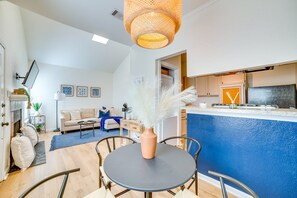 Ein modernes Wohnzimmer mit Sofa, Couchtisch und Sesseln, eine Küche mit blauer Spritzschutzwand und ein Essbereich mit Tisch und Stühlen.