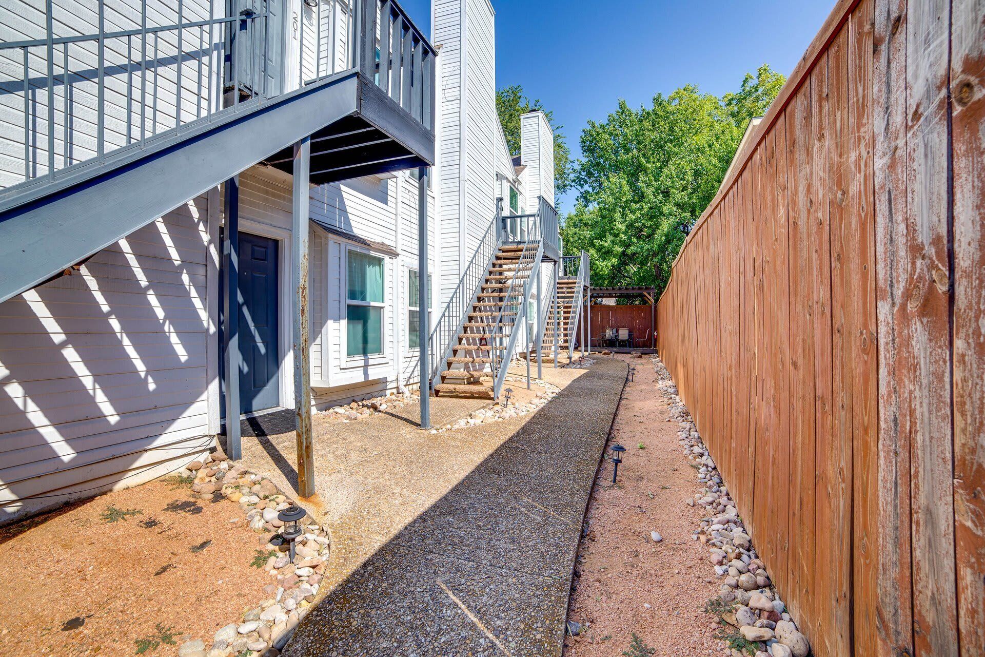A narrow pathway leading to a building with a metal staircase and a wooden fence.