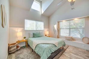 Ein Schlafzimmer mit einem Bett, zwei Nachttischen, einem Fenster mit Jalousien, einem Oberlicht und einem Teppich.