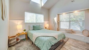 Een slaapkamer met een bed, twee nachtkastjes, een raam met zonwering, een dakraam en een vloerkleed.