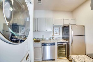 A compact kitchen with white cabinets, a stainless steel dishwasher, a built-in oven, and a refrigerator. - Modern Dallas Retreat (Dallas)