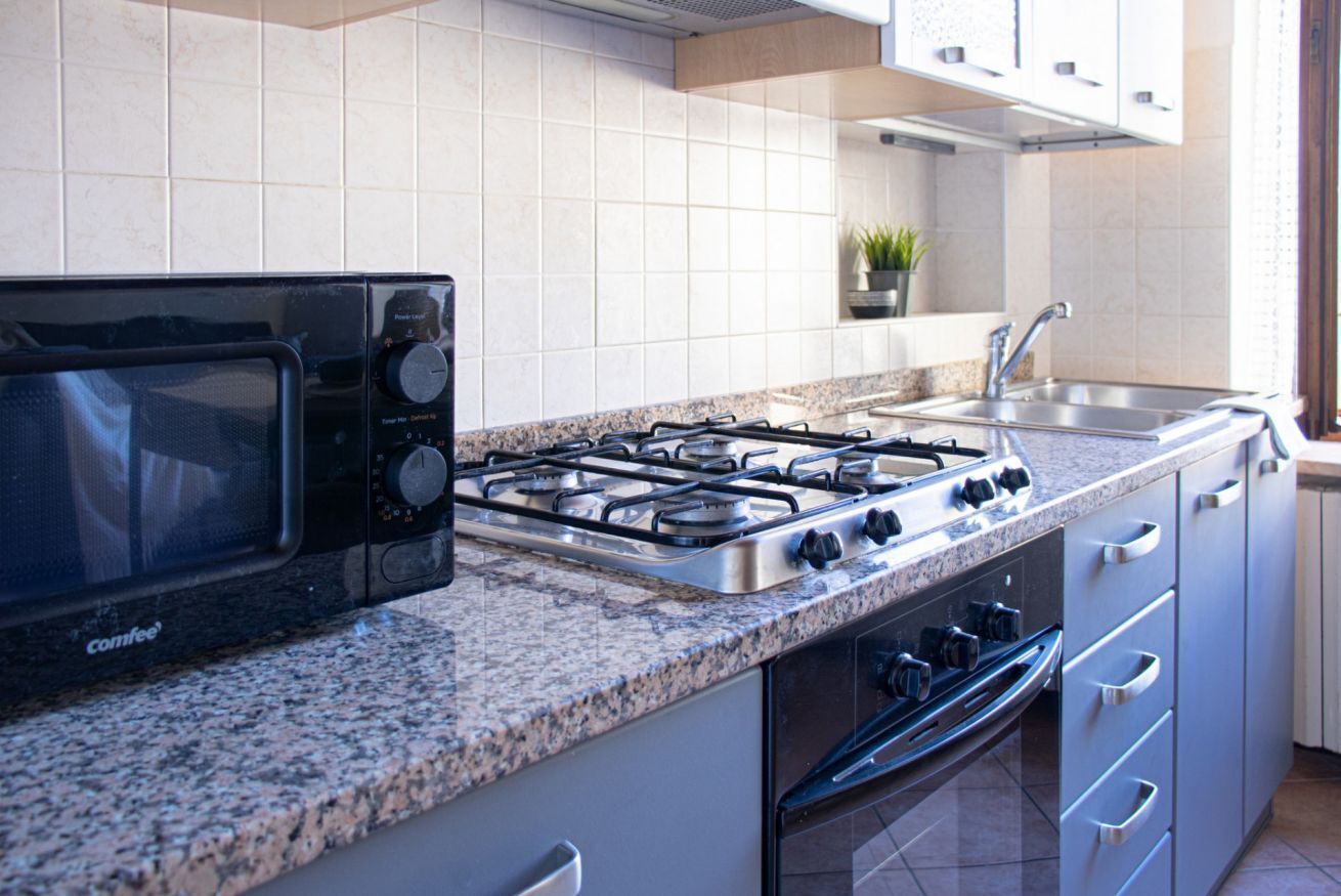 Eine Küche mit Mikrowelle, Gasherd, Backofen, einer Arbeitsplatte aus Granit, einer Spüle aus Edelstahl und einer weißen Küchenwand.