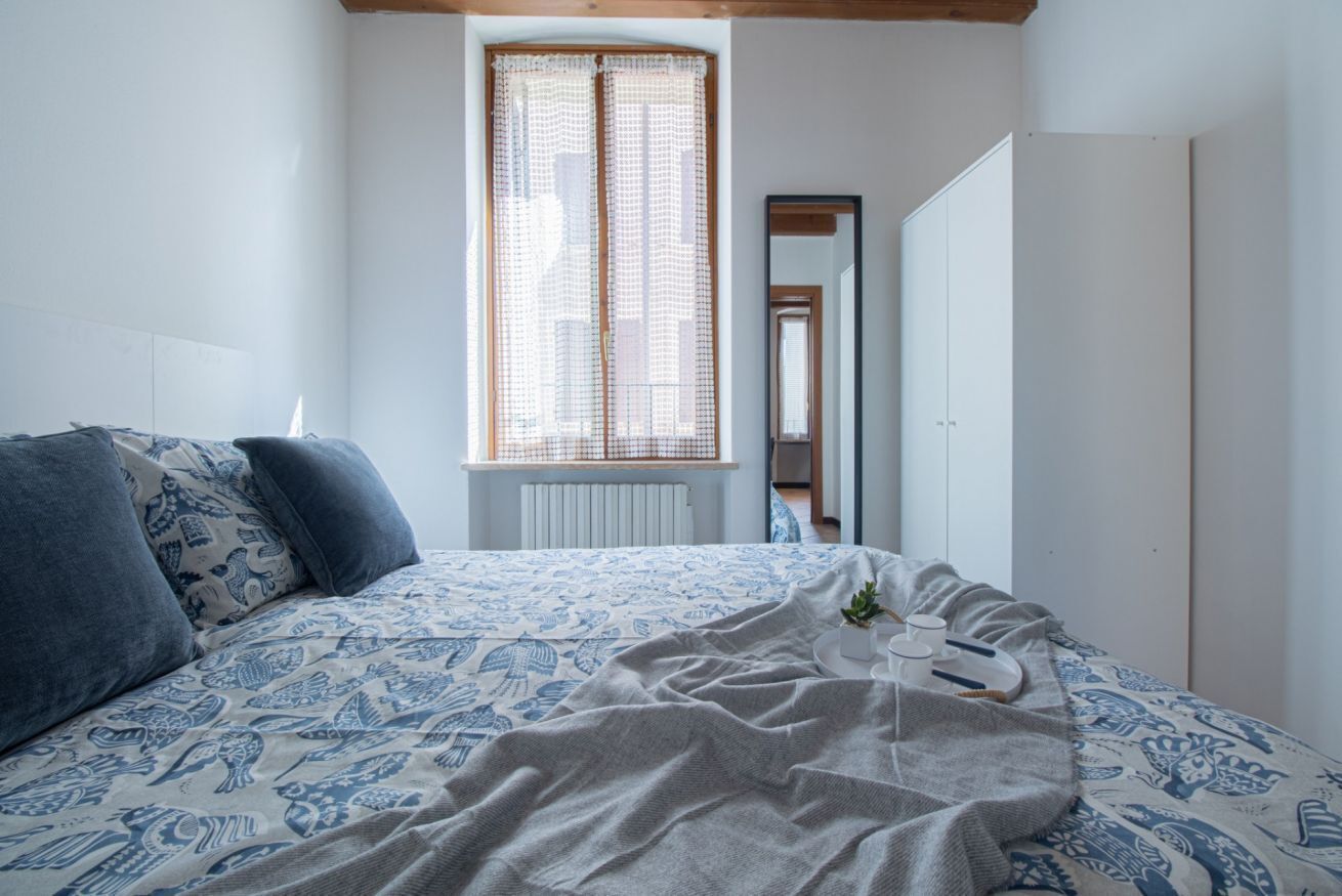 A bedroom with a bed, a window with curtains, a radiator, and a wardrobe.
