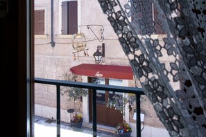 Ein Balkon mit rotem Markisenvorhang, Blumentöpfen und einem Gebäude mit brauner Tür und verrollten Fenstern.
