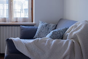 Ein Zimmer mit Fenster, Heizkörper und einer Couch mit Decke.