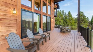 Una terraza de madera con sillas Adirondack, una mesa y una puerta de cristal que da a un espacio cubierto.