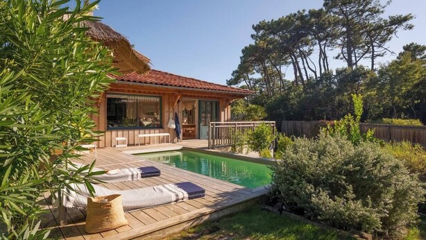 Ein Haus mit Swimmingpool, Holzterrasse und Sitzbereich im Freien.
