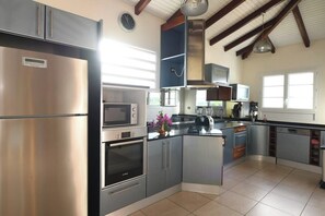A modern kitchen with stainless steel appliances, a microwave, oven, and a built-in island with a sink. - Upper Floor Villa  (sleeps 10) • Panoramic View & Pool (Rivière-Salée)