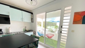A kitchen with a dining area, a sliding glass door to a balcony, and a view of a green landscape.