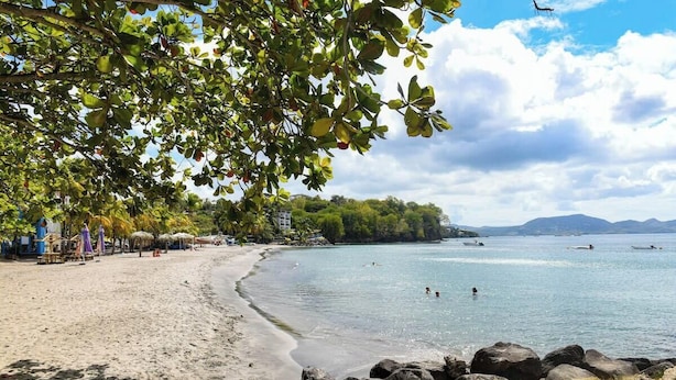 A beach with a sandy shore, calm water, and a row of beachside structures.