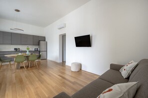 A modern living space with a dining area, kitchen, and a grey sofa with floral cushions. - GuestHost - Villetta Agapanto (Bari)