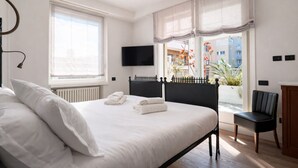 A modern bedroom with a large bed, a flat-screen TV, a view of a balcony with plants, and a cityscape. - Elegantis Terrazze al Vaticano - Your Chic Retreat in Central Rome (Roma)