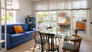 A room with a blue sofa, a glass table, and wooden chairs. - Elegantis Terrazze al Vaticano - Your Chic Retreat in Central Rome (Roma)