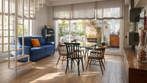 A modern living room with a blue sofa, wooden chairs, a glass table, and a kitchen visible through large windows. - Elegantis Terrazze al Vaticano - Your Chic Retreat in Central Rome (Roma)