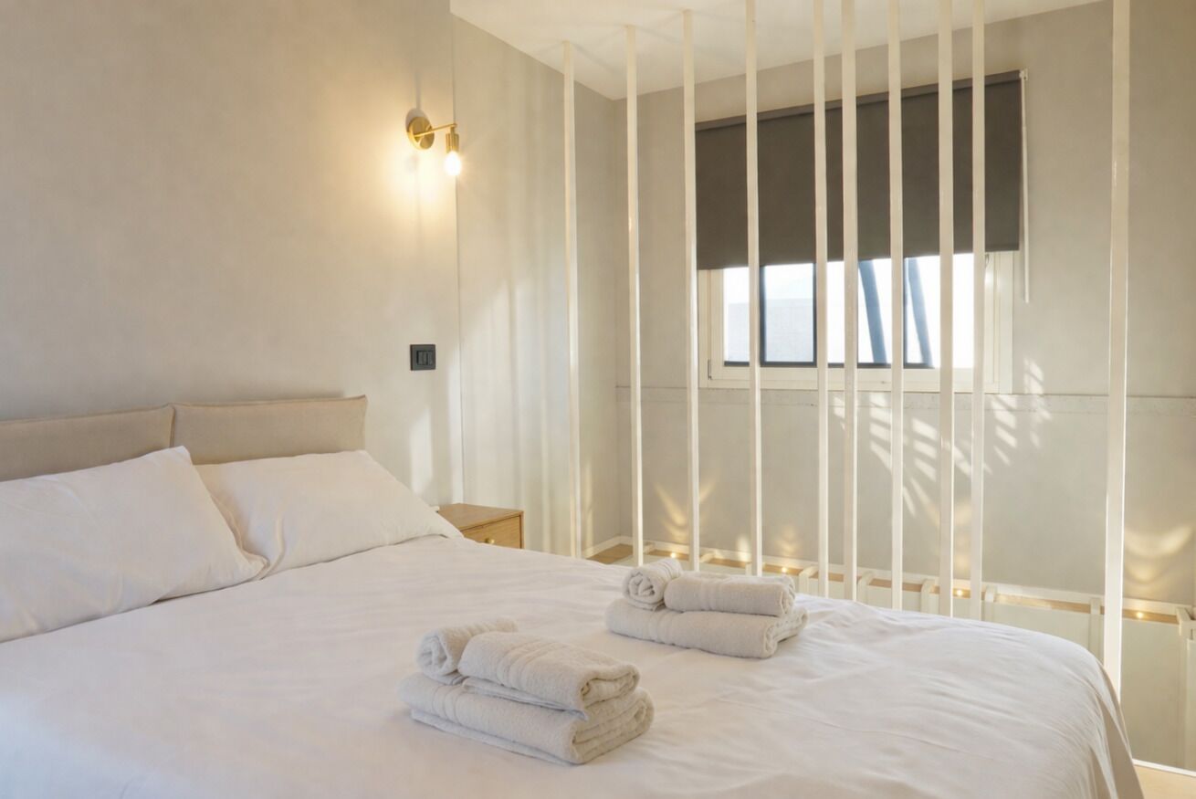 Una cama bien hecha con sábanas y toallas blancas, una mesita de noche y una ventana con persianas.
