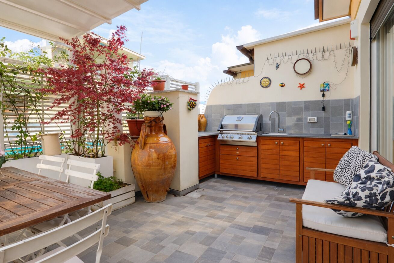 An outdoor kitchen with a grill, wooden cabinets, and a dining area with a table and chairs.