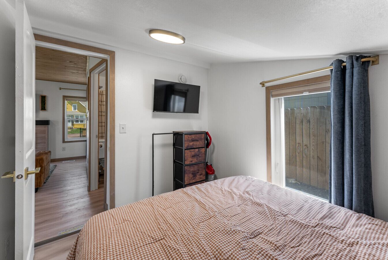 Un dormitorio con cama, televisor, armario y ventana con cortinas.