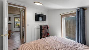 Un dormitorio con cama, televisor, armario y ventana con cortinas.