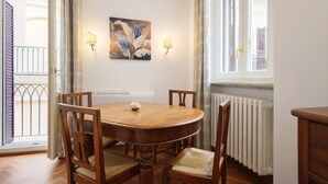 A dining room with a round wooden table, four chairs, two wall-mounted light fixtures, a painting, and a window with a view of a balcony. - Elegantis Pantheon Suite near Piazza Navona - Historic Centre (Roma)
