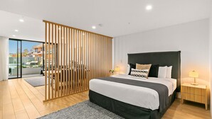 Un dormitorio moderno con una cama grande, un separador de madera y vistas a un edificio.