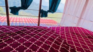 A bed with a patterned bedspread, a view of mountains through a window, and a ceiling fan. - Adventure trails (Kodaikanal)