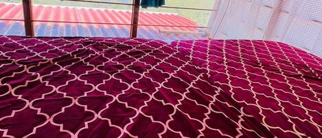 A bed with a patterned bedspread, a view of mountains through a window, and a ceiling fan.