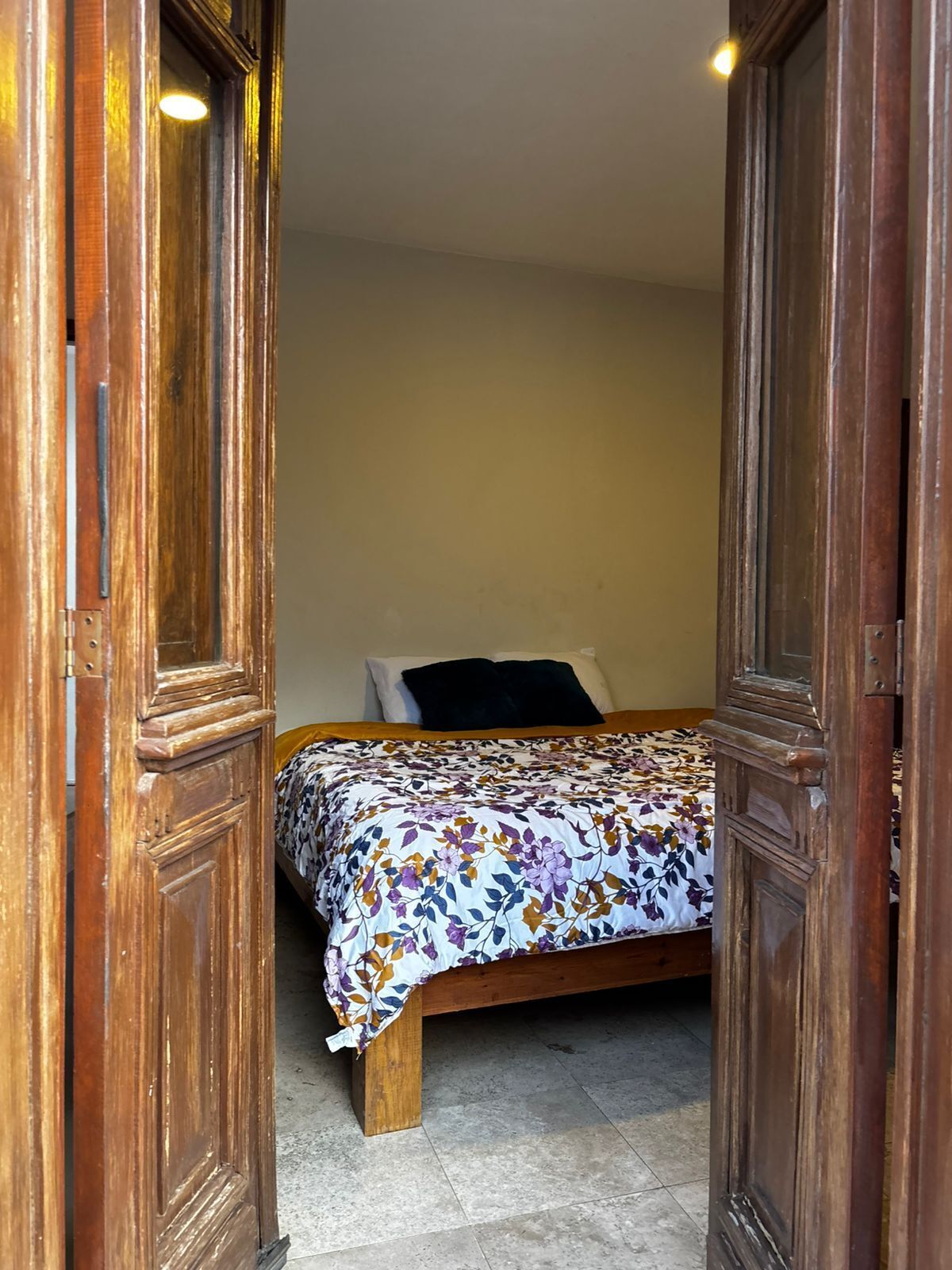 Una habitación pequeña con una cama, marcos de puerta de madera y suelo de baldosas.
