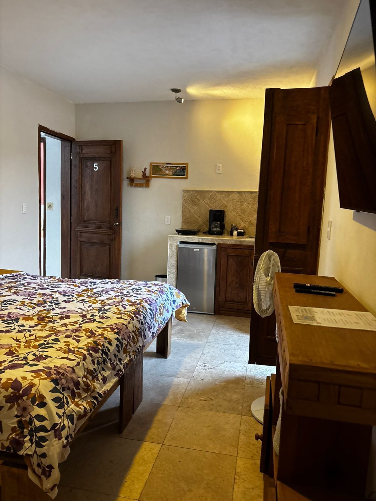 Een slaapkamer met een bed, een bureau, een stoel, een kleine kitchenette en een badkamer.