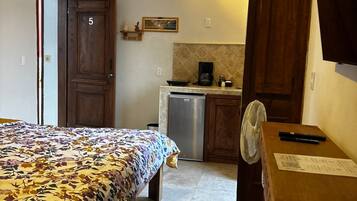 Een slaapkamer met een bed, een bureau, een stoel, een kleine kitchenette en een badkamer.