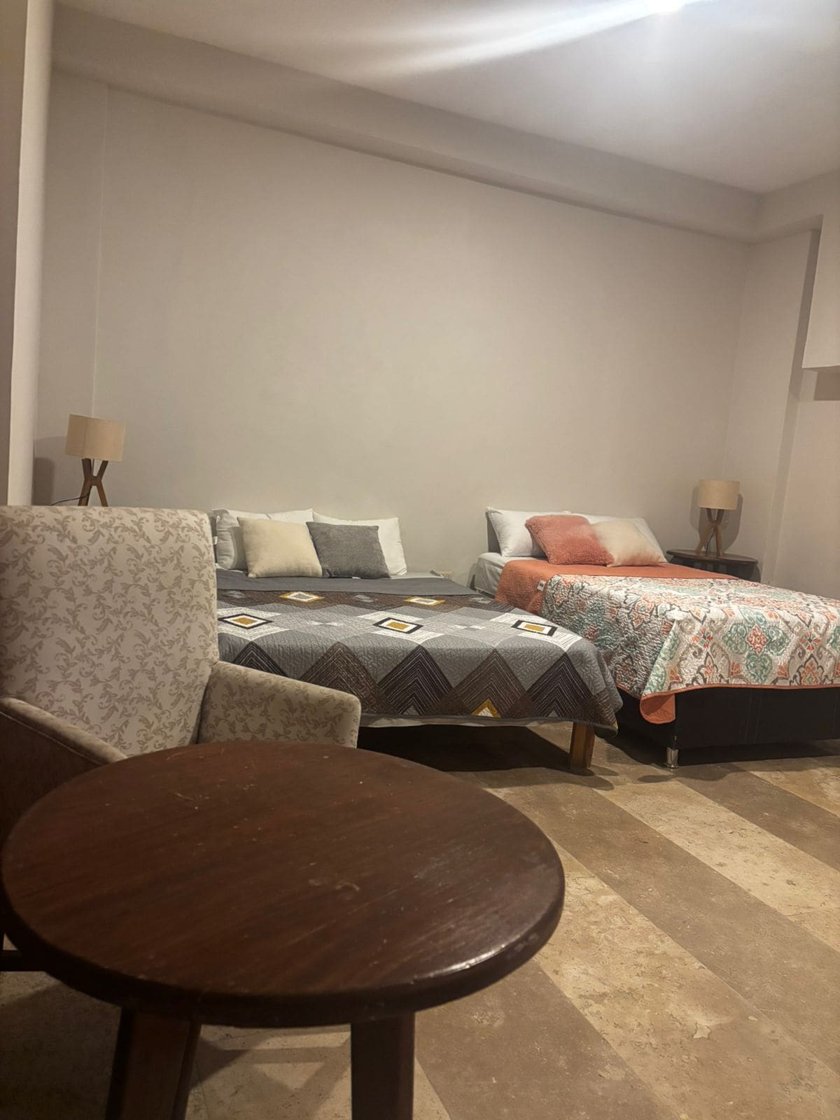 Quarto com duas camas, uma cadeira e uma mesinha.
