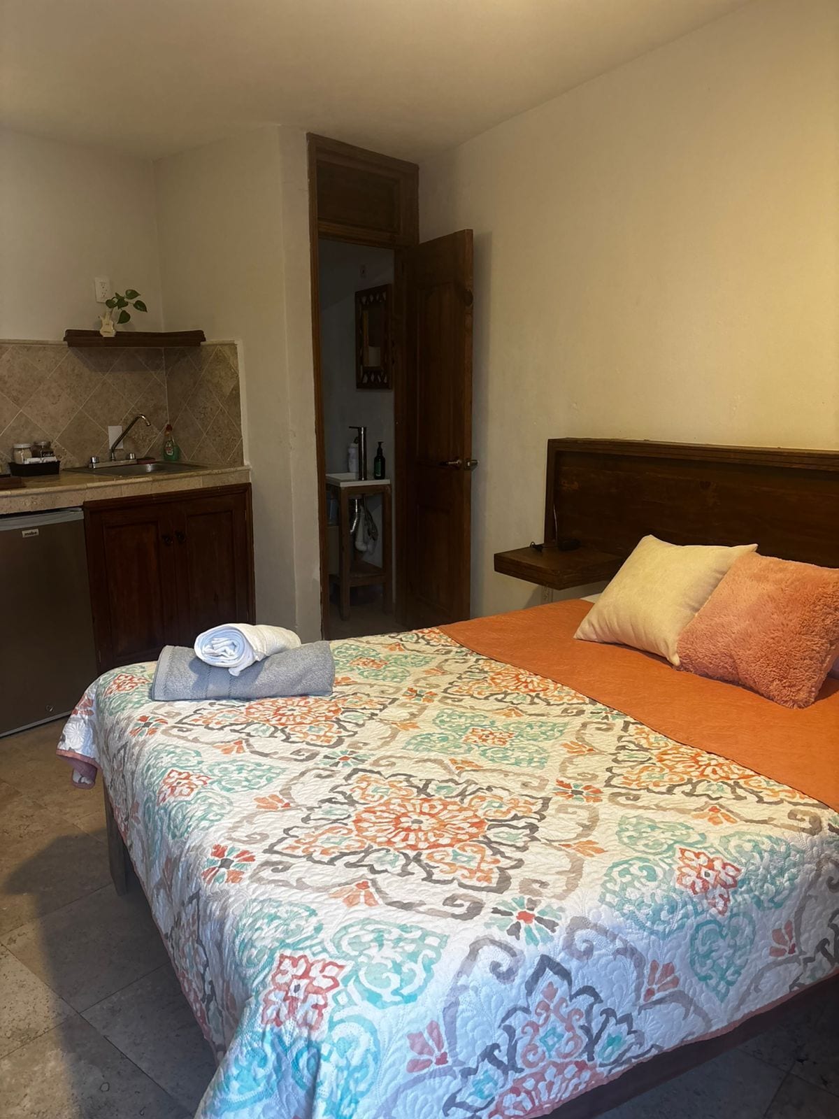 Un dormitorio con una cama, una mesita de noche, un aparador y un baño visible a través de una puerta abierta.
