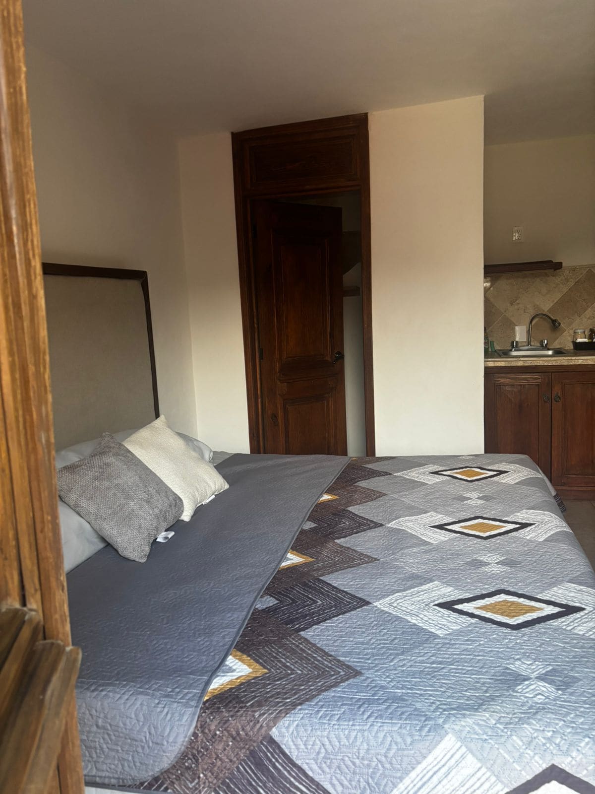 Un dormitorio con cama, una puerta de madera y una kitchenette al fondo.