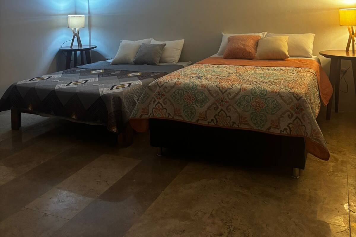 A bedroom with two beds, a nightstand, a lamp, and a ceiling light.