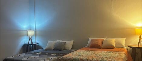 A bedroom with two beds, a nightstand, a lamp, and a ceiling light.