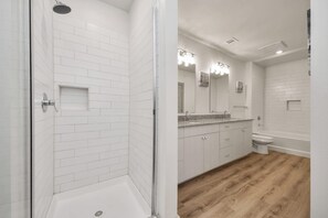 Ein Badezimmer mit weißen Fliesen, einer Dusche, einem Waschbecken und einer Toilette.
