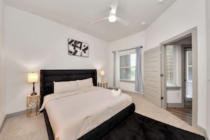 A bedroom with a bed, a ceiling fan, a window with blinds, and a door leading to another room. - Modern Houston Escape Bowling, Pool Table & Gym (Houston)