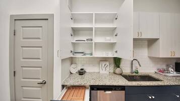 A kitchen with white cabinets, a granite countertop, a stainless steel dishwasher, and a white door.