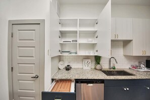 Una cocina con armarios blancos, encimera de granito, lavavajillas de acero inoxidable y una puerta blanca.