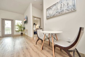 Una sala de estar moderna con una mesa redonda, dos sillas, una planta en maceta y un cuadro en la pared.
