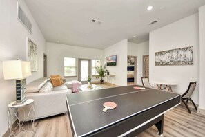 Amplia sala de estar con mesa de ping pong, un sofá, una mesa de centro y una mesa de comedor con sillas.