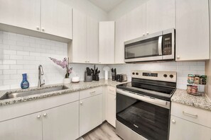 Una cocina moderna con armarios blancos, encimera de granito, electrodomésticos de acero inoxidable y microondas integrado.