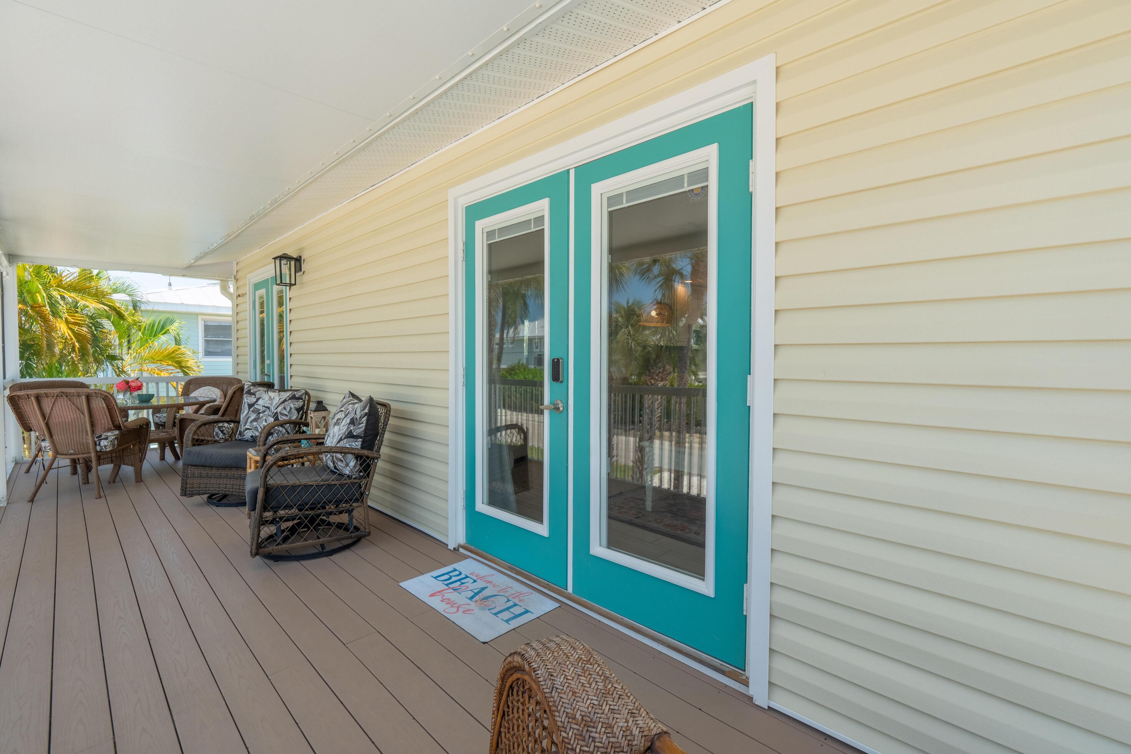 A covered porch with wicker furniture and a 'Beach' mat.